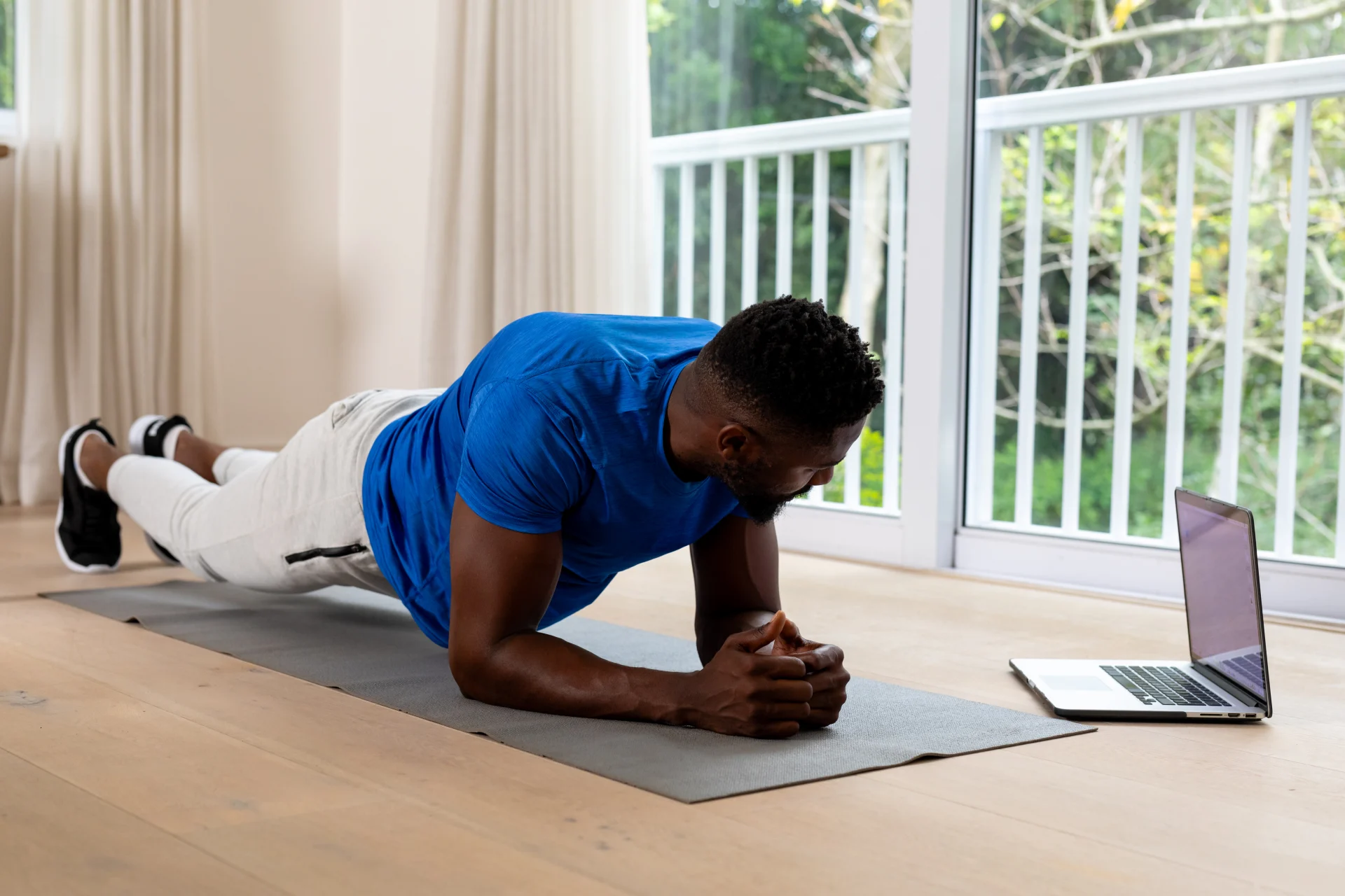 Un homme fait du gainage sur un tapis devant un ordinateur portable, à domicile.
